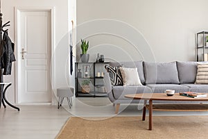 Wooden table on carpet in front of grey sofa in minimal living room interior with door