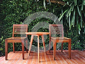 Wooden table and chair furniture with green tropical plant background in backyard garden.