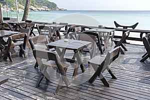 Wooden table and chairs in empty beach cafe next to sea water. Island Koh Phangan, Thailand