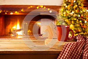 Wooden table with coffee cup over Christmas tree and fireplace background.  Christmas and New Year mock up for design and product