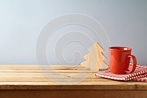 Wooden table with coffee cup and wooden Christmas tree over gray wall background.  Christmas and New Year mock up for design and