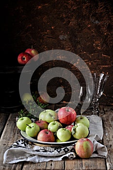 On a wooden table on a cotton towel a metal dish with fresh red and green apples