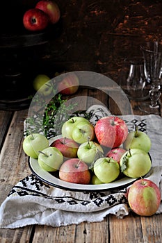 On a wooden table on a cotton towel a metal dish with fresh red and green apples