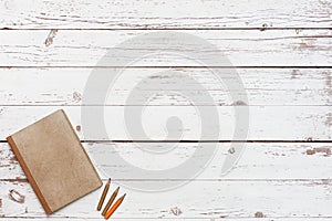 Wooden table with craft grunge notebook and a pencil in a corner, top view