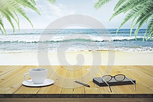 Wooden table with cup of coffee, eyeglasses and diary on the beach