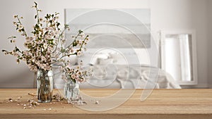 Wooden table, desk or shelf close up with branches of cherry blossoms in glass vase over blurred view of scandinavian white