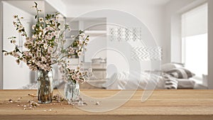 Wooden table, desk or shelf close up with branches of cherry blossoms in glass vase over blurred view of scandinavian white