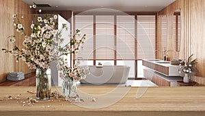 Wooden table, desk or shelf close up with branches of cherry blossoms in glass vase over view of wooden bathroom with bathtub and