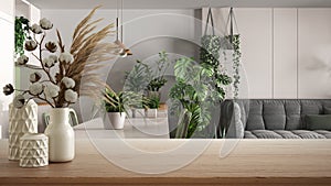 Wooden table, desk or shelf close up with ceramic vases with cotton flowers over modern kitchen and living room with houseplants,
