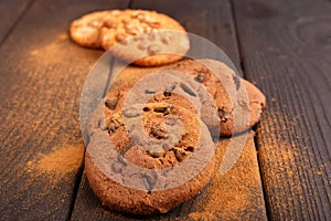 On the wooden table are a few oatmeal cookies and cookies with chocolate. Side view. Inside.