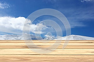 Wooden table, free space, your product or advertising text, snowy mountain peaks, blue sky and clouds, light colors