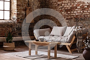 Wooden table in front of beige sofa in living room interior in wabi sabi style with plants and red brick wall photo