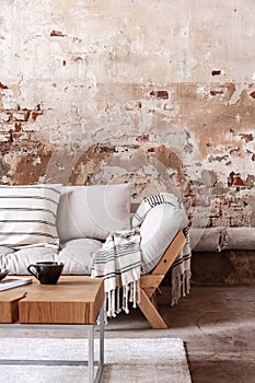 Wooden table in front of grey couch with blanket in wabi sabi living room interior with red brick wall
