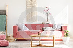 Wooden table in front of red sofa in pastel living room interior