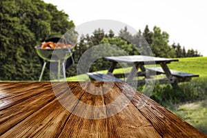 Wooden tabletop and blurred grill on grass and garden background.