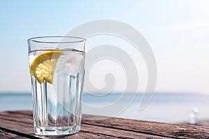 Wooden table with glass of refreshing lemon drink on hot summer day outdoors
