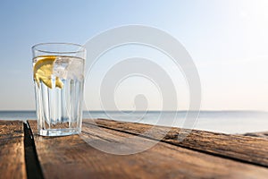 Wooden table with glass of refreshing lemon drink on hot summer day outdoors