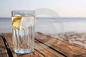 Wooden table with glass of refreshing lemon drink on hot summer day outdoors