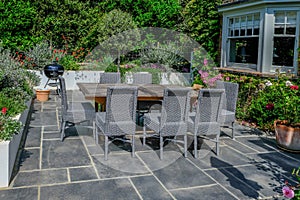 Wooden table and grey wicker chairs on a modern patio with a round bar-b-que in the background