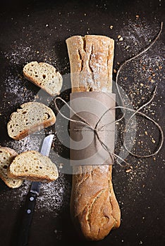 Wooden table with a knife, a loaf of fresh bread, and slices of the bread scattered on the surface