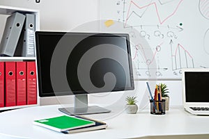 wooden table with laptop pc monitor pen andd other, whiteboard with business graph on wall