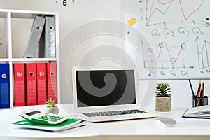 wooden table with laptop pc monitor pen andd other, whiteboard with business graph on wall