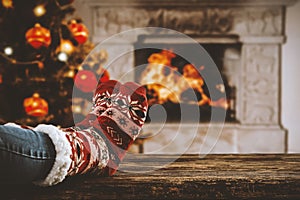 Wooden table with legs in christmas socks with fireplace background and space for your decoration, products and text.