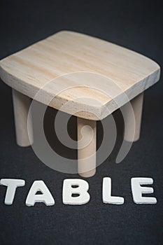 Wooden table with lettering on black background furniture toy doll house model natural material decor design vertical image