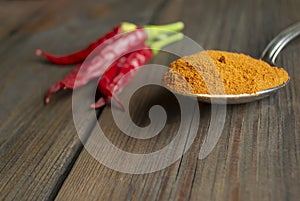 On a wooden table lies fresh hot peppers next to crushed chili powder in a spoon. Chopped hot peppers next to pods from