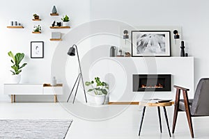 Wooden table next to grey armchair in white interior with poster