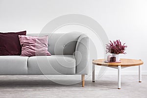 Wooden table next to grey settee with purple pillows in grey apartment interior. Real photo