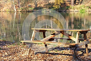 Wooden table with picnic benches in the open air on the background of fallen oak leaves near a forest lake