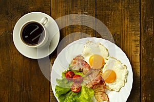 On a wooden table is a plate with fried eggs and a cup of coffee.