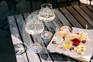 A wooden table in a restaurant with a cheese plate, grape, honey bread and white wine. Wine glasses and cheese served