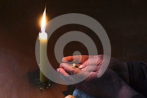 Wooden table in retro style. On it is a candle and a cross. Hands of an old woman over a book. Palms folded