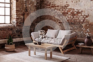 Wooden table on rug in front of beige couch in apartment interior in wabi sabi style with red brick wall