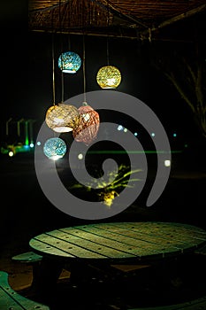 wooden table with seats placed in garden lights and wooden roof with tree and lights in background