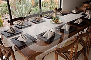 Wooden table set for dinner with cross back chairs with lush green garden in the background
