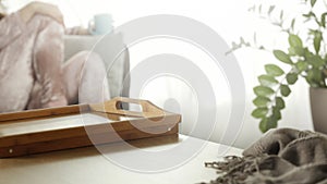 Wooden table with space for your product or text. Blurred bright nice cozy home interior background. Blurred woman on the sofa.