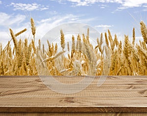 Wooden table surface over defocused golden wheat field landscape background