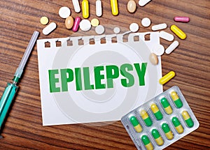 On a wooden table, a syringe, pills and a sheet of paper with the inscription EPILEPSY. Medical concept