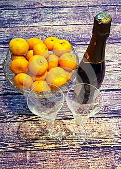 on a wooden table tangerines in a crystal vase, wine glasses and a bottle of champagne