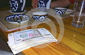 On a wooden table a tea set with a traditional ornament and a large bundle of sums money the currency of Uzbekistan, focus on mo