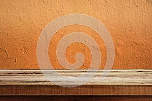 Wooden table and texture of orange color cement wall background.
