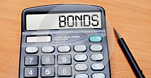 On a wooden table there is a black pen and a calculator with the text BONDS. Business concept