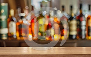 Wooden table top and beautiful bokeh shelves with alcohol bottles at the pub background. Bar concept