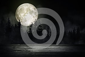 Wooden table top with forest in the dark night and fog or mist with full moon in background.