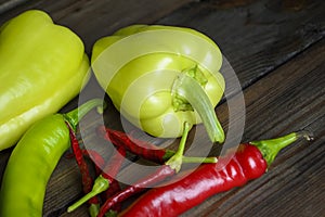 On a wooden table are two bell peppers, a hot green pepper, a hot red pepper and a lot of small chilies. Different types of pepper