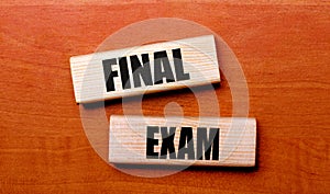 On a wooden table are two wooden blocks with the text FINAL EXAM photo