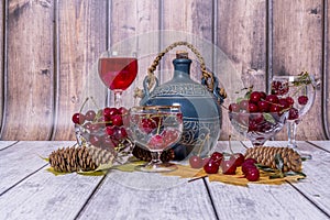 Vase with ripe cherries, jug and glass of wine, yellow maple leaves lie on wooden table.